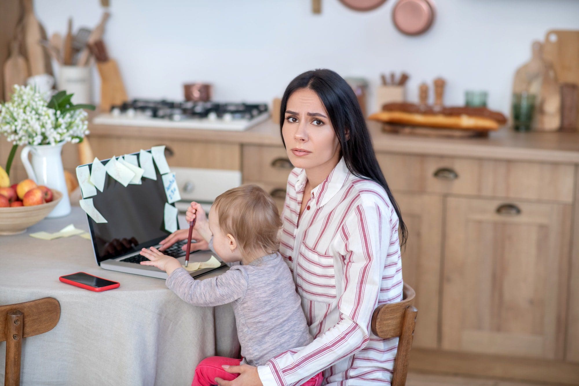 Stressed mom sitting with daughter, trying to manage her work